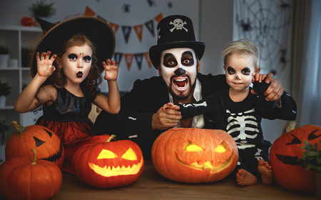 padre de familia e hijos en disfraces y maquillaje para halloween con calabaza en la oscuridad en el hogar