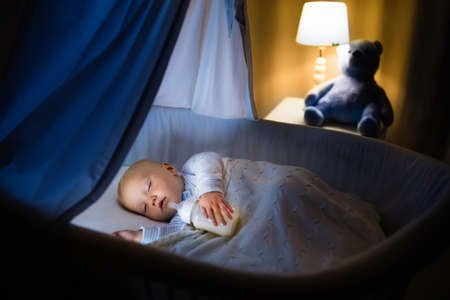 かわいい赤ちゃんが夜天蓋付き青バシネットで牛乳を飲みます ベビーベッド ランプ おもちゃのクマと暗い部屋で寝る 準備式のボトルとパジャマの少年 子供のためのベッド時間ドリンク の写真素材 画像素材 Image