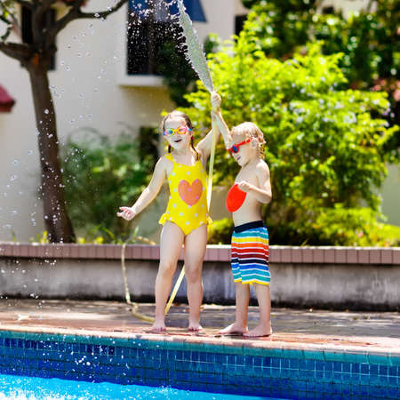 大きな屋外スイミングプールのある裏庭でガーデンホースで遊ぶ子供たち