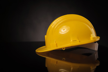 side view of a yellow construction safety  helmet on a black table with reflexion