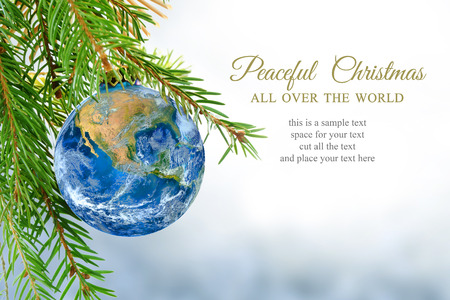 earth globe as christmas ball hanging on fir branch, message: peaceful Christmas all over the world, symbol, metaphor, copy space, bright snowy background.