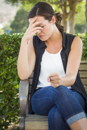 sad lonely: Upset Young Woman Sitting Alone on Bench Outside with Her Head in Her Hand and Clenched Fist.