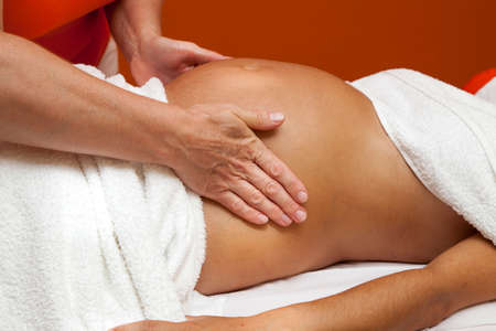 Massage: Беременная молодая Латина женщина с красивой кожи, завернутые в полотенце, лежа на кровати и имеющие расслабляющий дородовой массаж, различные методы Фото со стока