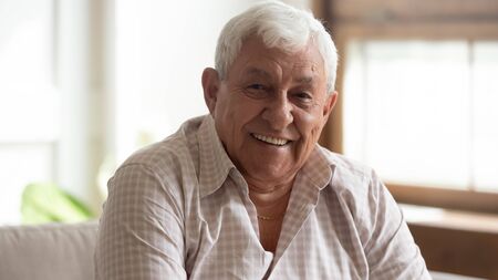 Close up headshot portrait of smiling mature man sit on couch at home look at camera posing, happy senior male feel optimistic uplifted demonstrate healthy positive elderly lifestyle concept Stock Photo