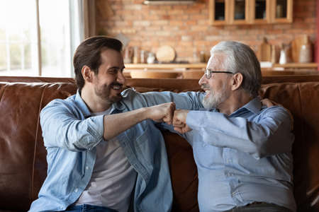 Réjouis-toi mon garçon. souriant amical mature grand-père papa jeune adulte petit-fils enfant se détendre sur un canapé confortable donner un coup de poing. aimer deux générations de famille, le fils adulte et le père aîné expriment l'unité de liaison