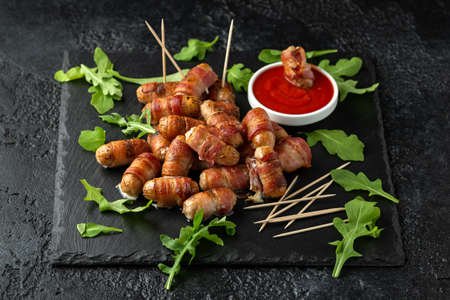 Party finger food pigs in blankets on toothpicks with ketchup sauce and wild rocket leaves