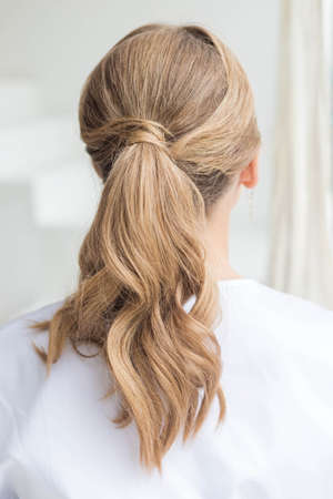 A young woman with long blond wavy hair tied in a ponytail. back view. Banco de Imagens