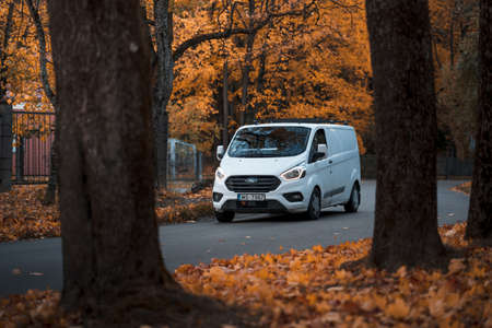 Riga, latvia-october 6, 2021: white ford transit custom commercial vehicle driving on the city street during the beautiful autumn leaf fall