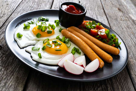 Petit-déjeuner - œuf au plat, saucisses bouillies et légumes servis sur une table en bois