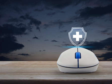 Cross shape with shield flat icon on wireless computer mouse on wooden table over sunset sky, business healthy and medical care insurance online concept 版權商用圖片