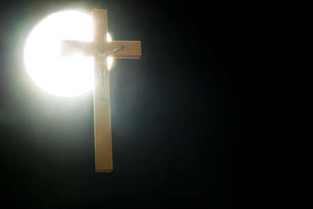 A crucifix against a round white light, against a black background - 114900212