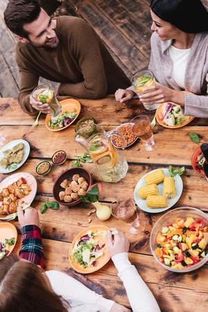 Abendessen mit besten Freunden. Draufsicht von vier Leuten, die zusammen beim Sitzen am rustikalen Holztisch zu Abend essen