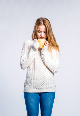 Stock Photo Teenage Girl In Jeans And White Sweater Holding A Cup With Hot Drink Young Woman Studio Shot On Gray Background Stock Photo Teenage Girl In Jeans And White Sweater Holding A Cup With Hot Drink Young Woman Studio Shot On Gray Background