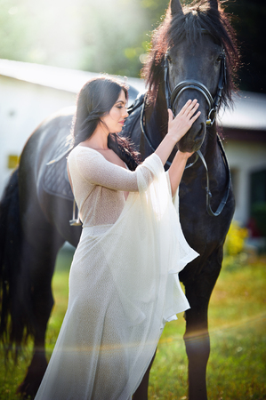 señora de moda con el vestido de novia blanco cerca de caballo
