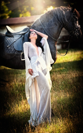 señora de moda con el vestido de novia blanco cerca de caballo