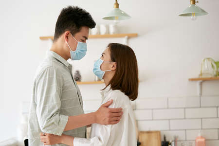 Side view of young asian couple wearing mask holding and looking at each other Фото со стока