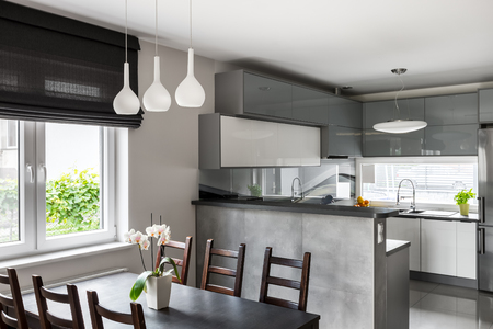 Simple dining set, decorative pendant lamp and roller blinds, light open kitchen in the background Фото со стока