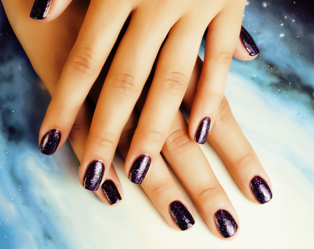 Manicure stylish concept: woman fingers with nails purple glitter on nails like cosmos, universe background