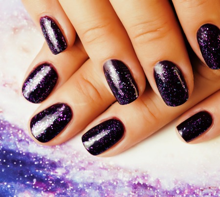 Manicure stylish concept: woman fingers with nails purple glitter on cosmos background Stock Photo