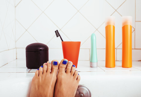 Woman legs in bathroom with lot of stylish stuff for care, pedicure creative design, hygiene spa mani pedi concept close up