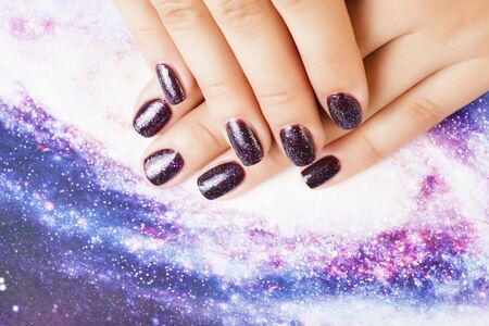 Manicure stylish concept: woman fingers with nails purple glitter on nails like cosmos, universe background closeup