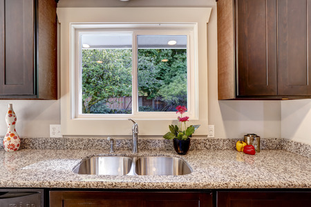 Dark brown kitchen cabinet with sink and granite counter top. View of backyard through the window