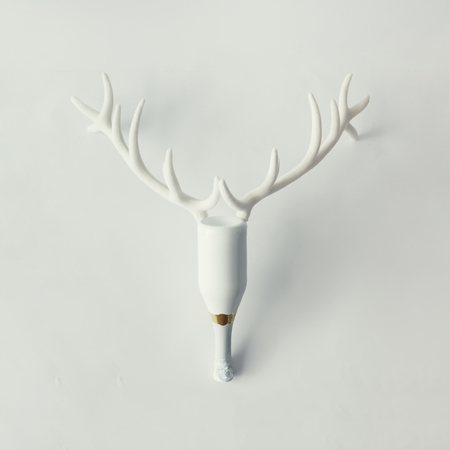 White Champagne bottle with reindeer antlers on bright background. New year party concept. Stock Photo