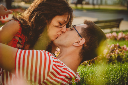 close up of lovely couple lying on green grass in park kissing
