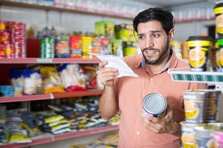 Nice man is choosing conserved peas with help note list in market
