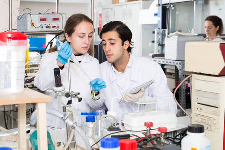 Two fine lab technicians discussing while working with reagents in test tubes during chemical experiment Stock Photo