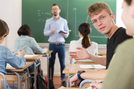 Boy and girl are sitting at the desk and talking in time lecture in the classroom