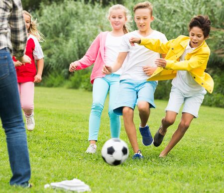 Cheerful happy children are jogning and playing football in the park.