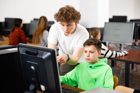 Teenager helps friend solve problem on computer in school class
