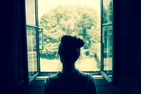 sad lonely: Woman looking through the window on the garden or forest in the countryside. Vintage filter. Blue tone. Stock Photo