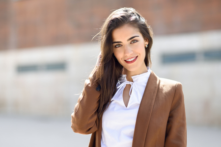 事務所ビル外に立っている素敵な髪を持つ若い女性 ウェーブのかかった髪型でフォーマルな服装を身に着けている実業家 茶色のジャケットとズボンを持つ少女 の写真素材 画像素材 Image