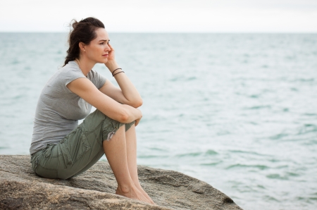 A sad and depressed woman sitting by the ocean deep in thought 