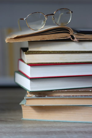 Stack of books on the table reading glasses and e reader on the table bookshelf in the background selective focus