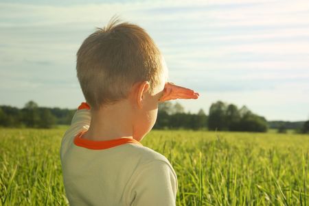 happy young boy looking horizon and dreaming on green field grass