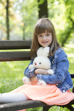Little girl sits on a bench in the park and holding in the hands of her favorite stuffed toy