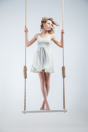 Young bare-footed girl on swing looking looking left. isolated over the white background. Stock Photo