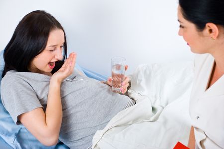 Young pregnant woman taking pills in hospital and being assisted  by a nurse - 6960509