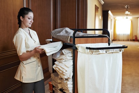 Hotel room service. female housekeeping worker with bedclothes linen in cart - 28668695