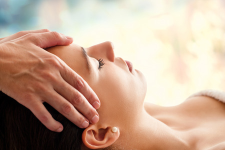 Massage: Закрыть голову портрет молодой женщины, имеющие массаж лица в спа-салоне. Терапевт массажа головы женщины против красочный фон. Фото со стока