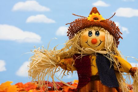 A scarecrow sitting on fall leaves on a sky background, scarecrow - 5630210