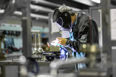 Industrial worker with protective mask welding inox elements in steel structures manufacture workshop. Фото со стока