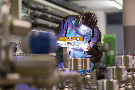 Industrial worker with protective mask welding inox elements in steel structures manufacture workshop. Фото со стока