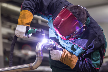 Industrial worker with protective mask welding inox elements in steel structures manufacture workshop. Фото со стока