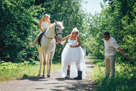 hombre, mujer vestida como una novia, niña y caballo blanco en el