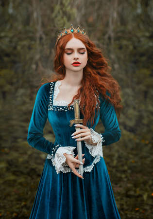 Militant fantasy red-haired woman queen holding dagger in hands. girl warlike princess warrior with sharp blade knife. red curly hair flying in wind. antique medieval lady countess. vintage blue dress