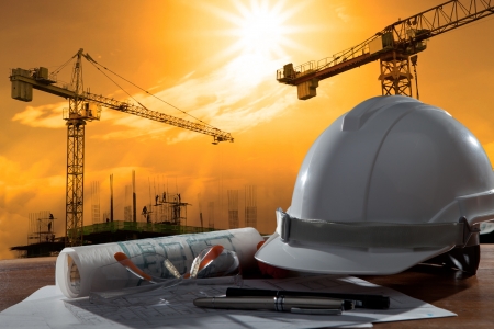 Archivo del casco de seguridad y pland arquitecto en la mesa de madera con escena de la puesta del sol y la construcción de edificios Foto de archivo - 22167832